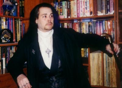 Rhys-Michael Silverlocke seated in front of his bookshelves